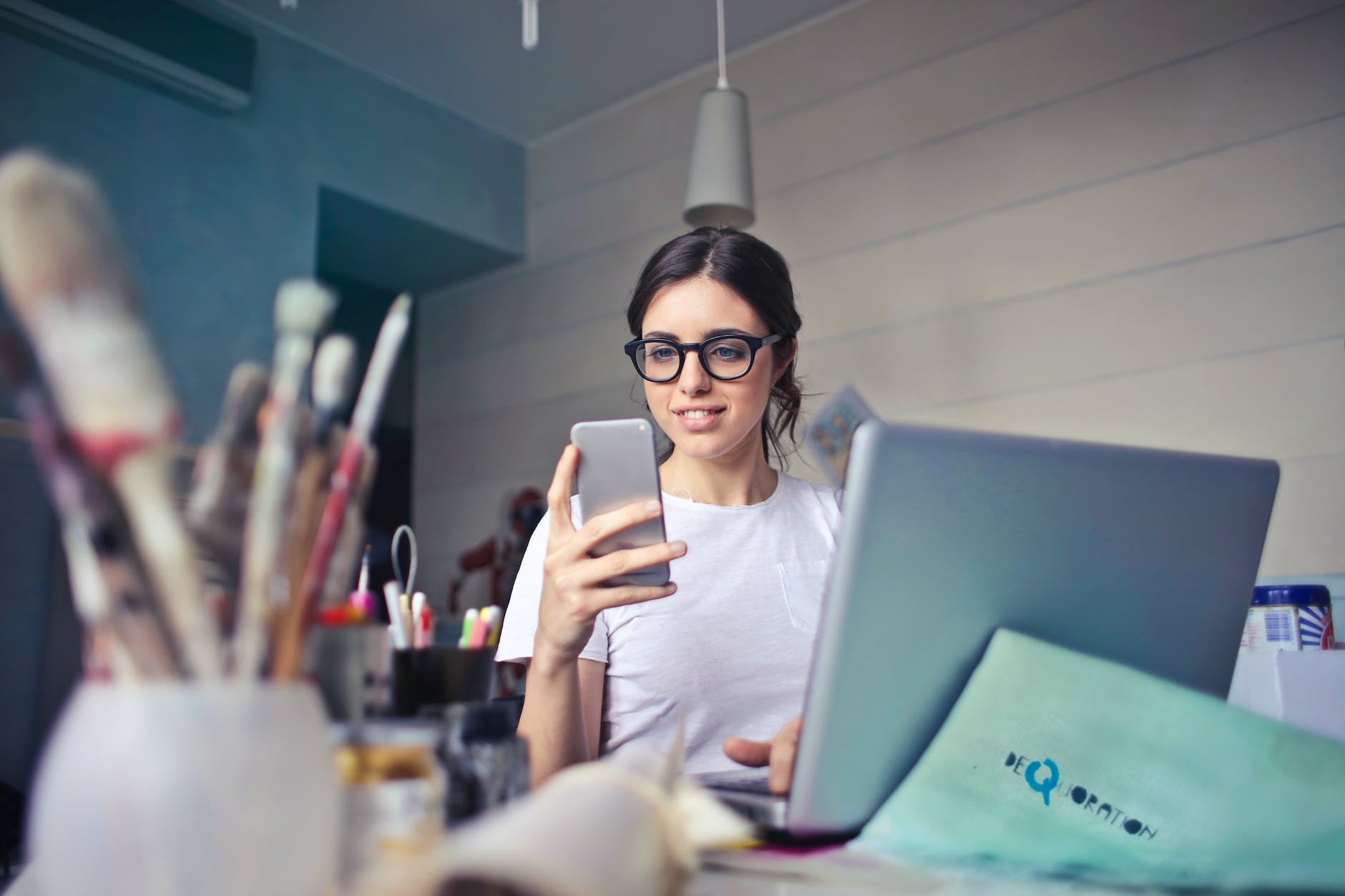 woman in white t shirt holding smartphone in front of laptop - running small business